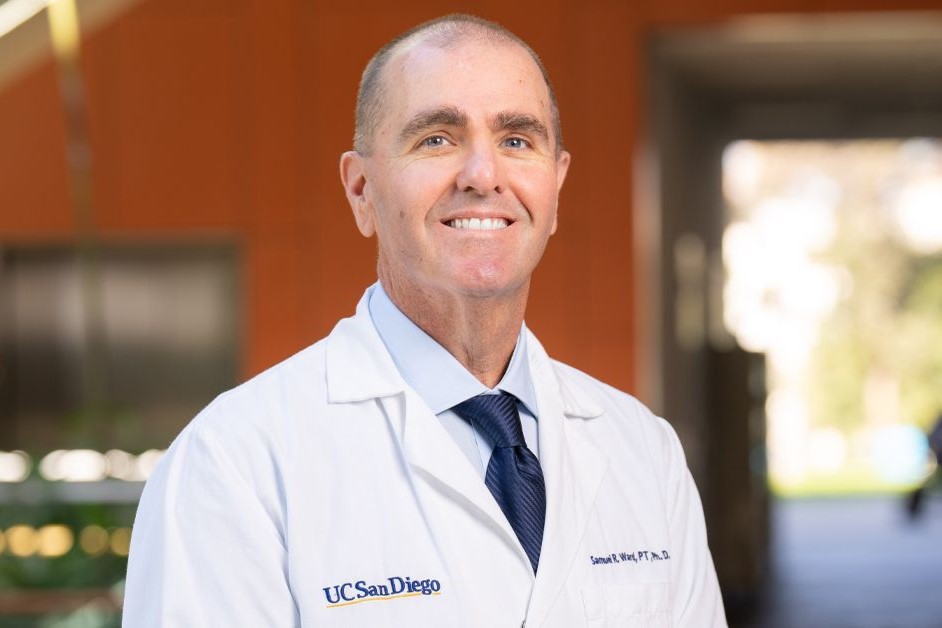 Dr. Sam Ward smiles in a doctor's white coat